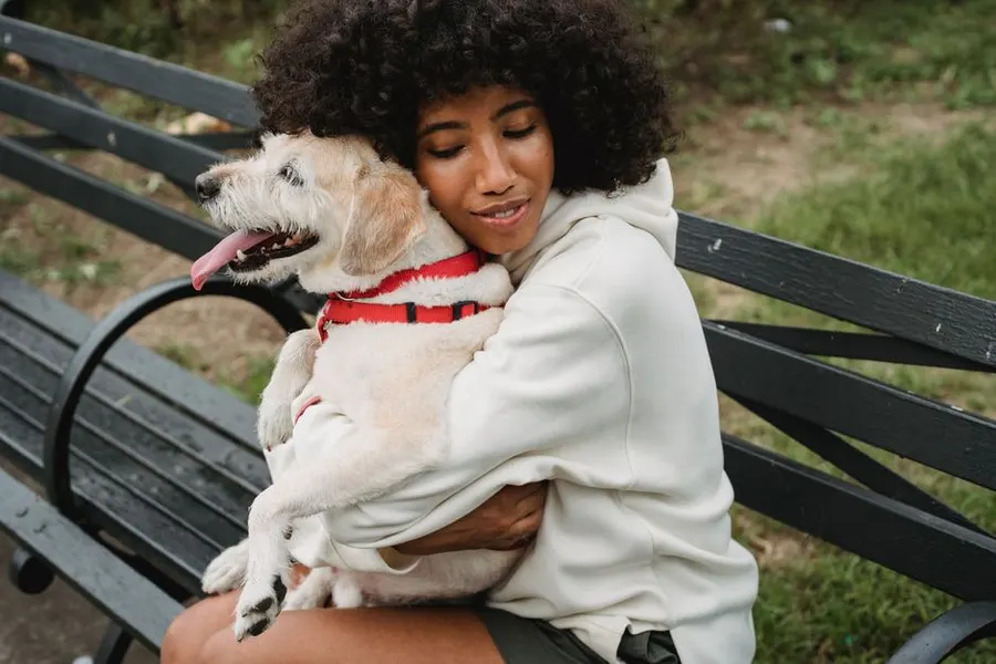 A young woman on a park bench hugs her fluffy white dog