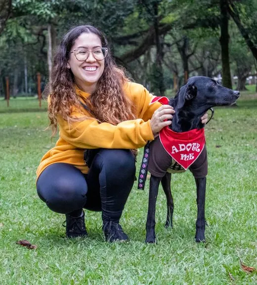 A woman crouches beside her dog in a red bandana on the grass